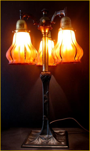 Title: Art Nouveau Lamp - Description: Three raisin coloured, flared shades look like flames when lit, atop a beautifully cast chestnut leaf adorned lamp base. Early 1900s art nouveau.